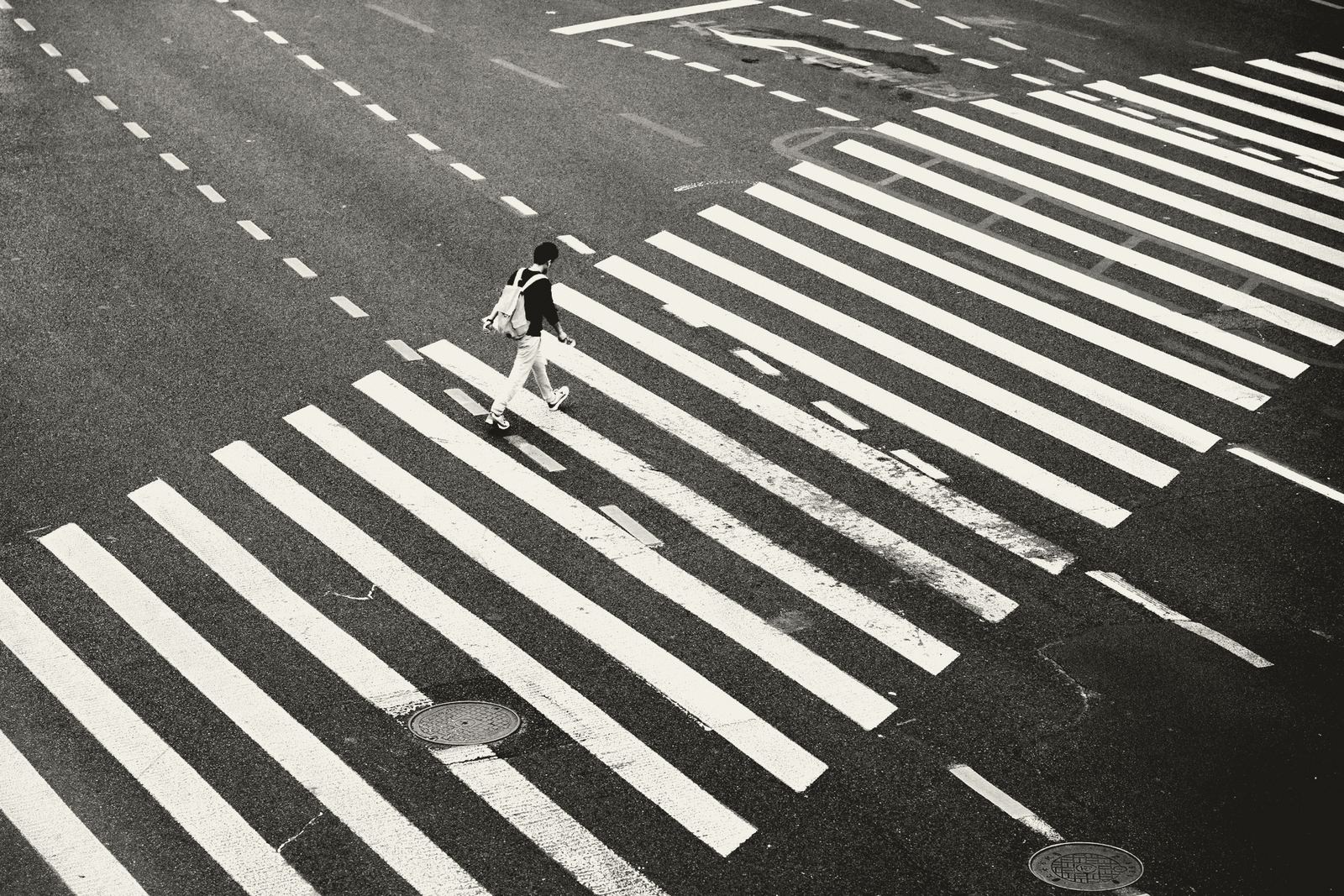 A lone pedestrian on a broad zebra crossing, seen from above